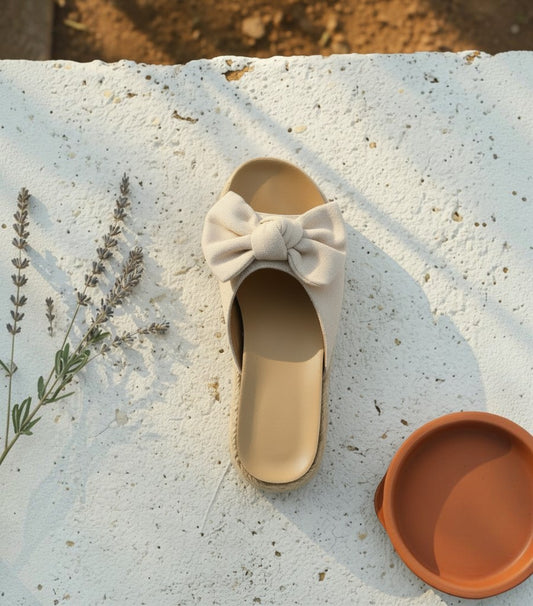 Alpargatas Clarvyna de cuña en color beige con detalle de lazo frontal sobre superficie de piedra natural