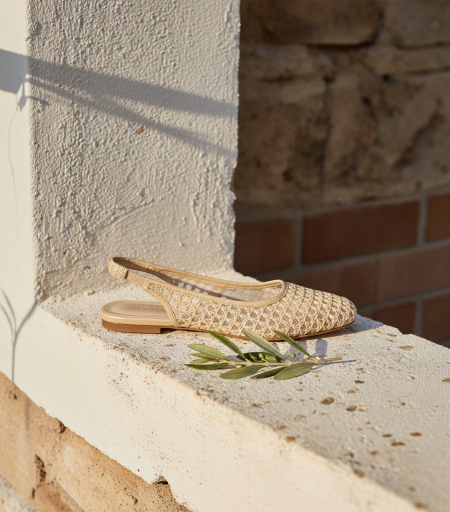 Bailarinas Clarvyna de tejido calado beige con tira trasera elástica y suela plana sobre un muro de piedra
