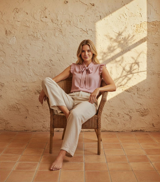 Modelo con blusa Clarvyna rosa de lunares con volantes y lazo al cuello, sentada en una silla de mimbre.