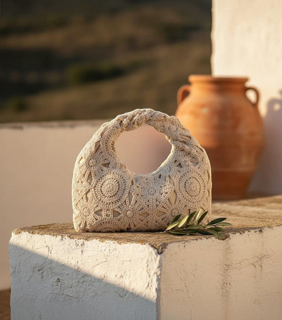 Bolso de rejilla Clarvyna en color beige con diseño de crochet floral y asa trenzada sobre un muro de piedra