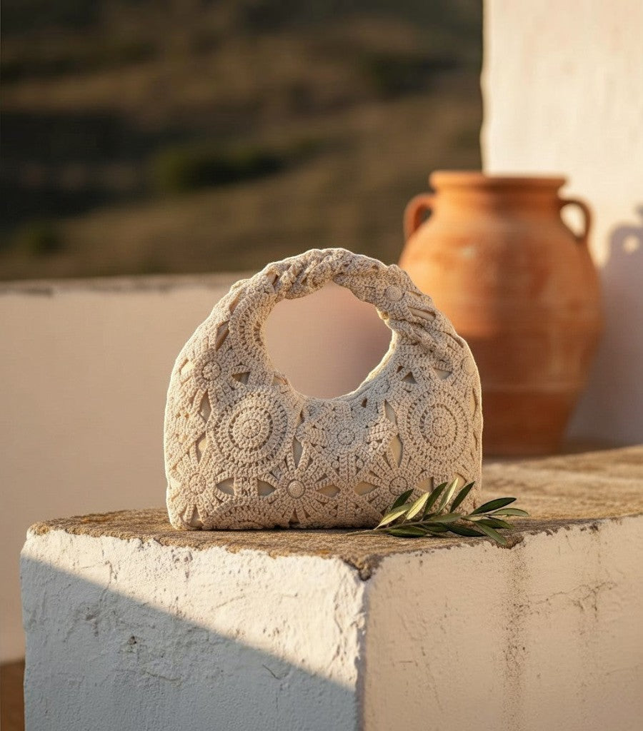 Bolso de rejilla Clarvyna color beige con diseño de crochet floral y asa trenzada sobre un muro de piedra rústico.