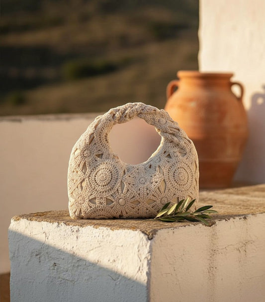 Bolso de rejilla Clarvyna color beige con diseño de crochet floral y asa trenzada sobre un muro de piedra rústico.