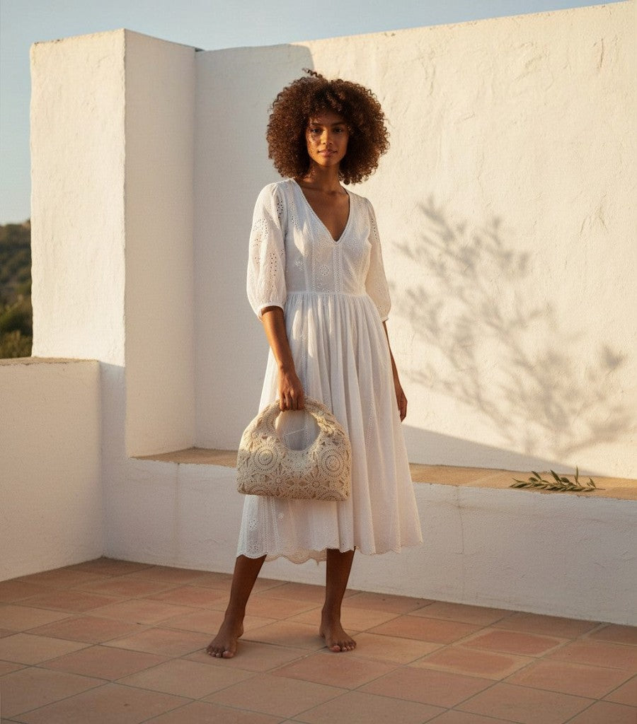 Modelo con vestido blanco y bolso de rejilla Clarvyna de crochet beige en una terraza al atardecer