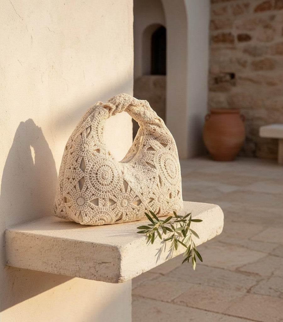 Bolso de rejilla Clarvyna color crema con diseño de crochet floral sobre un soporte de piedra en un patio rústico.