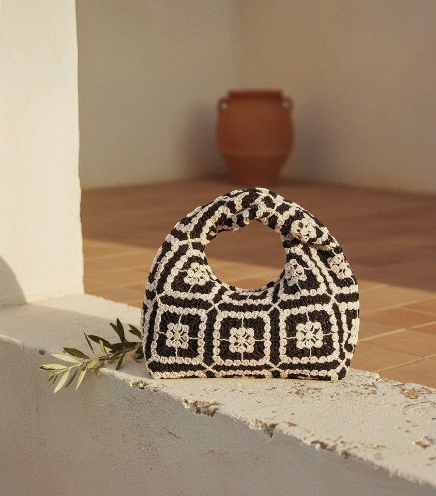 Bolso de rejilla Clarvyna con patrón de ganchillo en blanco y negro, diseño geométrico artesanal sobre muro de piedra.