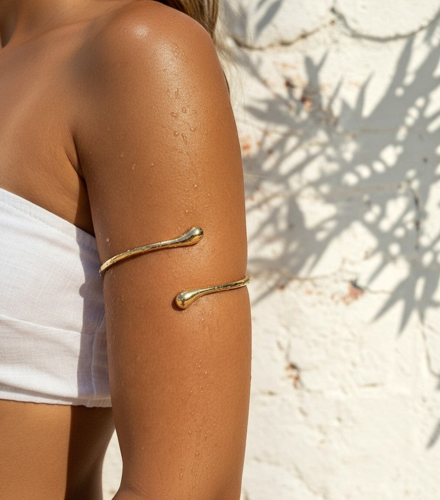 Brazalete Clarvyna de metal dorado con diseño de gota minimalista colocado en el brazo de una mujer