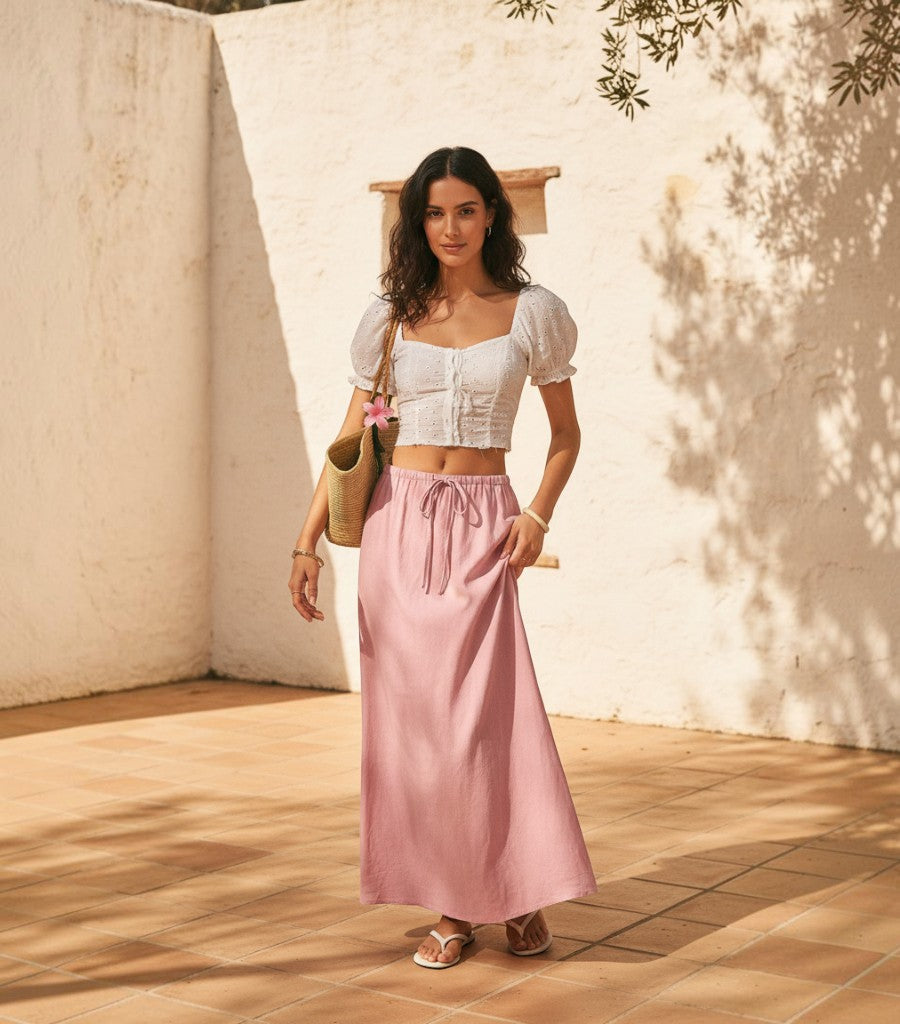 Falda midi Clarvyna de lino rosa con cintura ajustable, combinada con crop top blanco y bolso de rafia