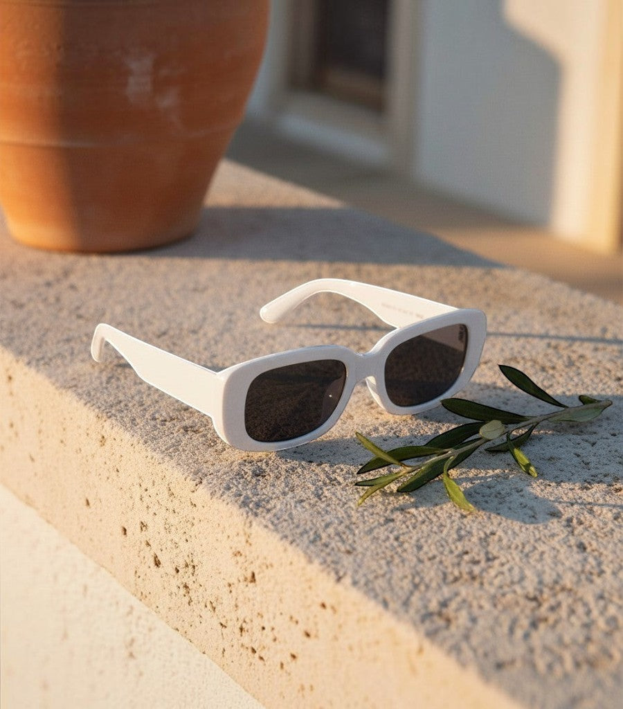 Gafas de sol cuadradas Clarvyna en color blanco con lentes oscuras sobre un muro de piedra al atardecer