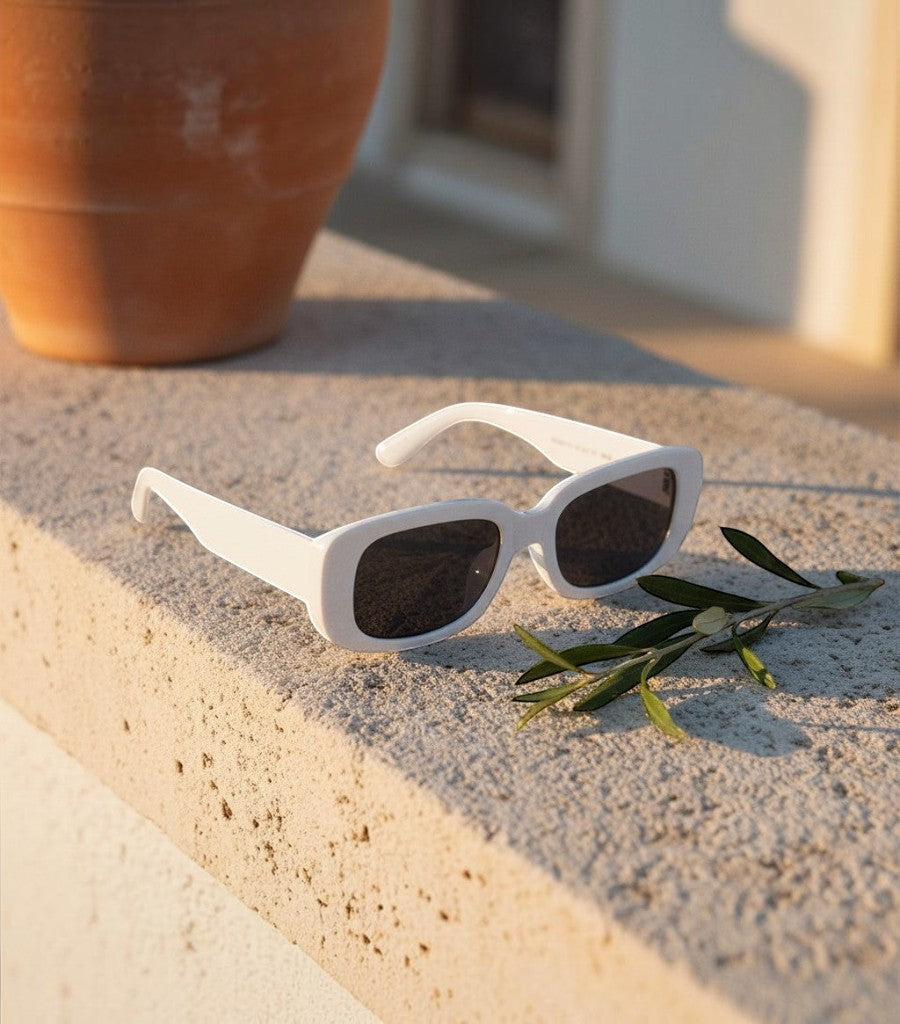 Gafas de sol cuadradas Clarvyna blancas con montura de tendencia sobre un muro de piedra al atardecer