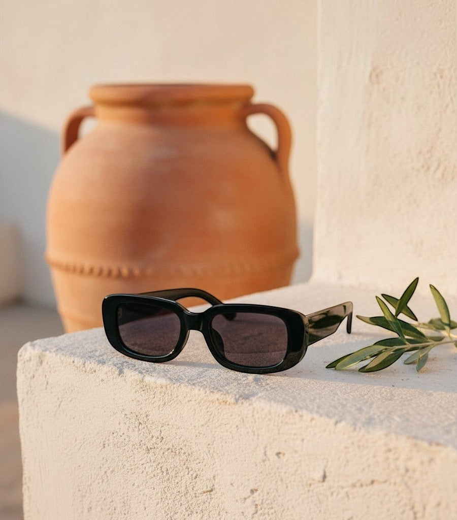 Gafas de sol cuadradas negras Clarvyna con montura de acetato sobre una superficie de piedra con una vasija de fondo