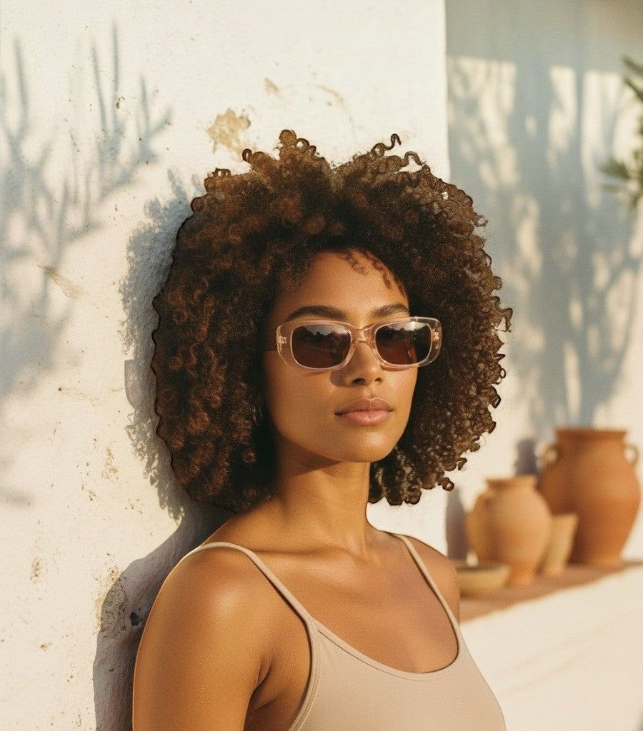 Mujer con gafas de sol cuadradas Clarvyna de montura transparente y cristales marrones en un entorno soleado