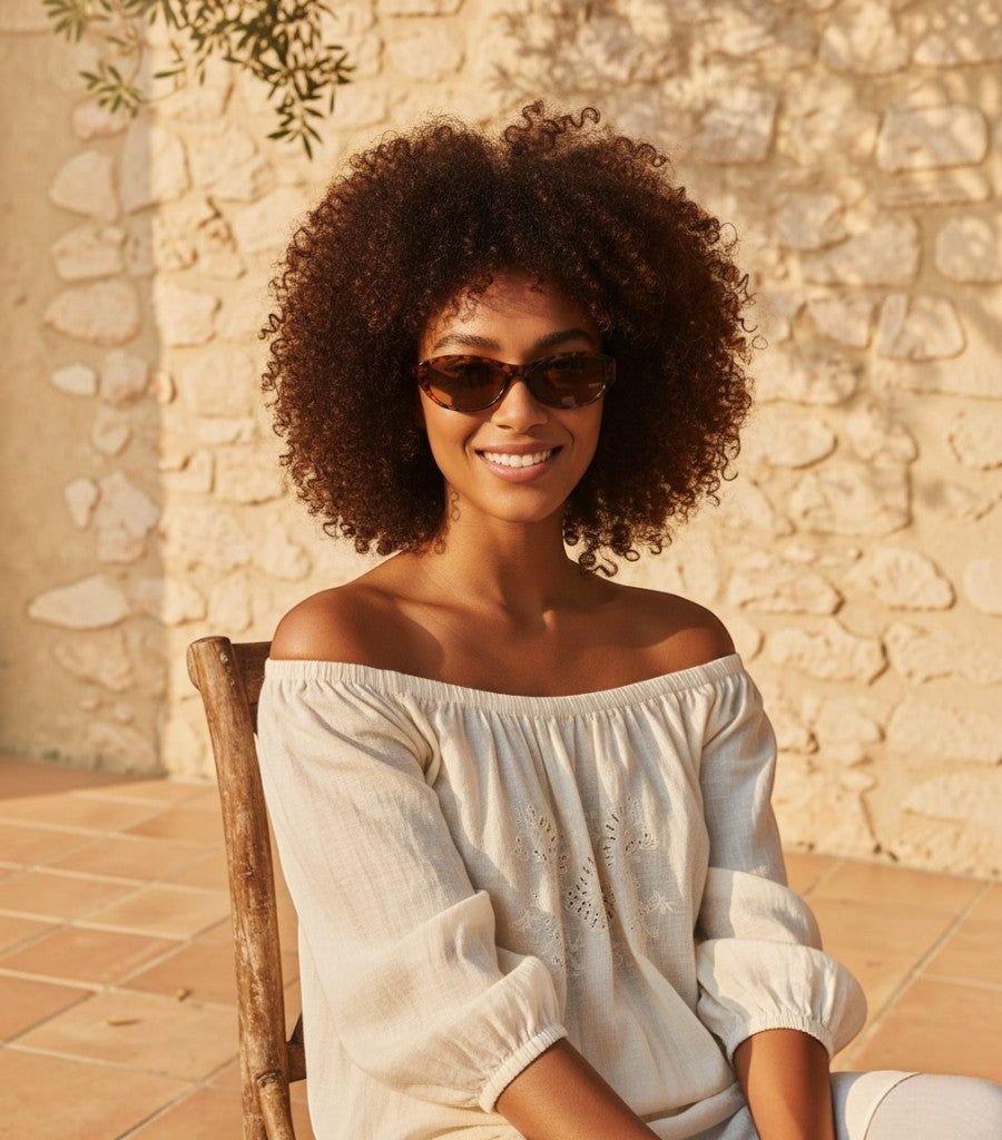 Mujer con gafas de sol Clarvyna de montura ovalada estilo retro y estampado carey en un entorno soleado
