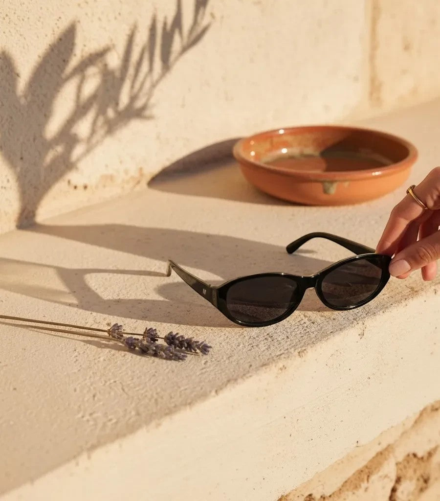 Gafas de sol Clarvyna con montura ovalada negra de estilo retro sobre una superficie de piedra al sol