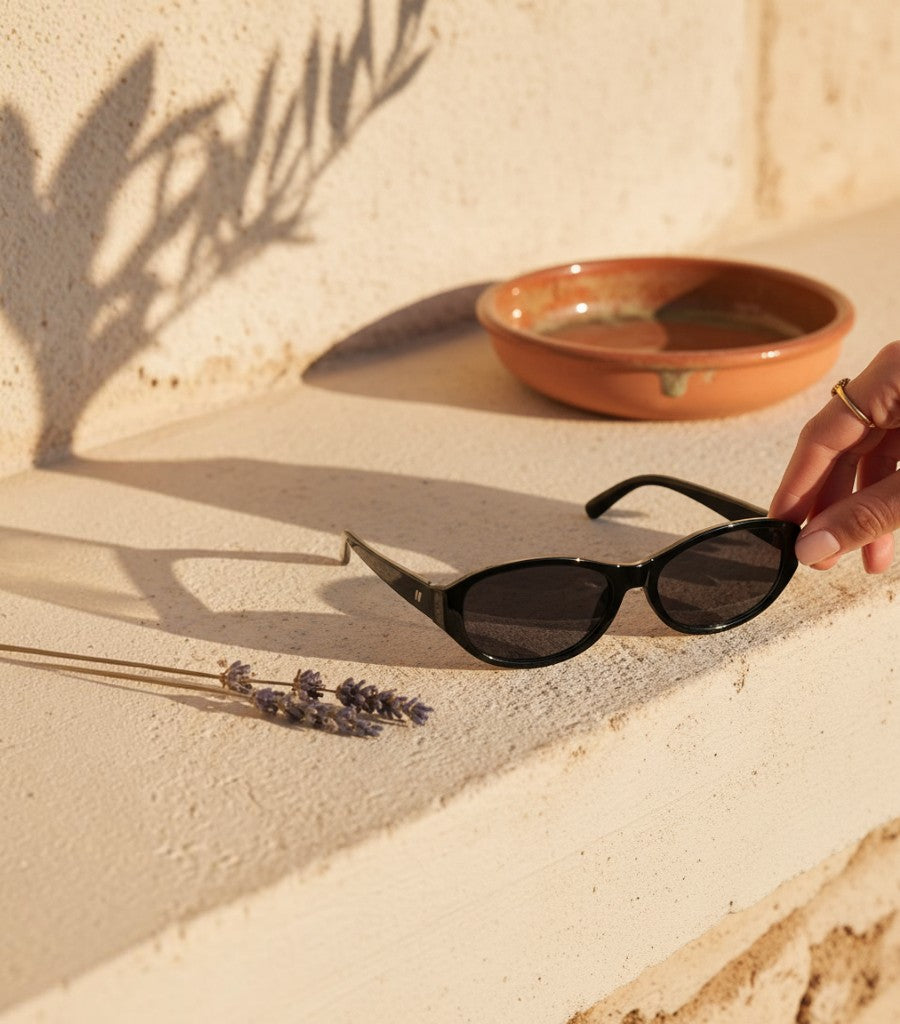 Gafas de sol Clarvyna con montura ovalada negra de estilo retro sobre una superficie de piedra al sol