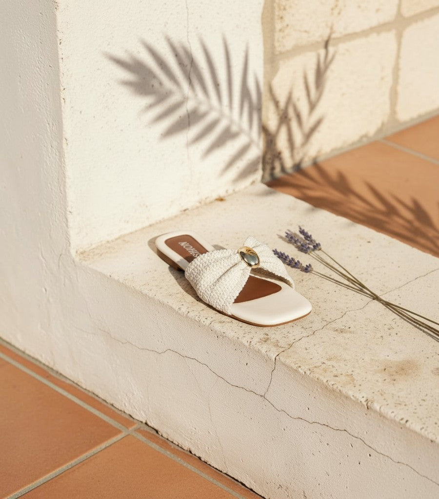 Sandalias planas Clarvyna de color crema con tira trenzada artesanal y detalle metálico central sobre piedra