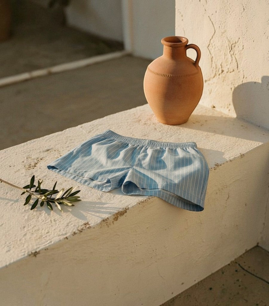 Short boxer Clarvyna de rayas azules y blancas en tejido ligero sobre un muro de piedra al sol con una vasija