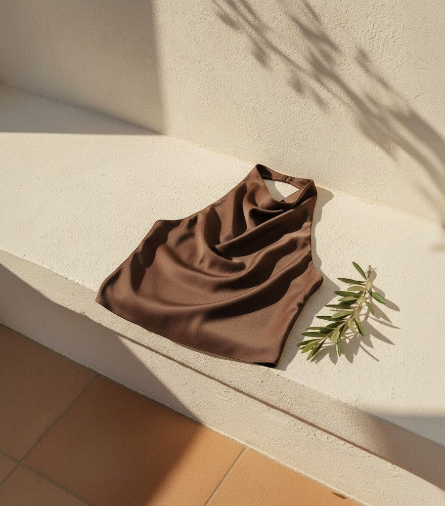 Top corsé halter de satén marrón Clarvyna, diseño elegante y fresco ideal para verano sobre una superficie de piedra.