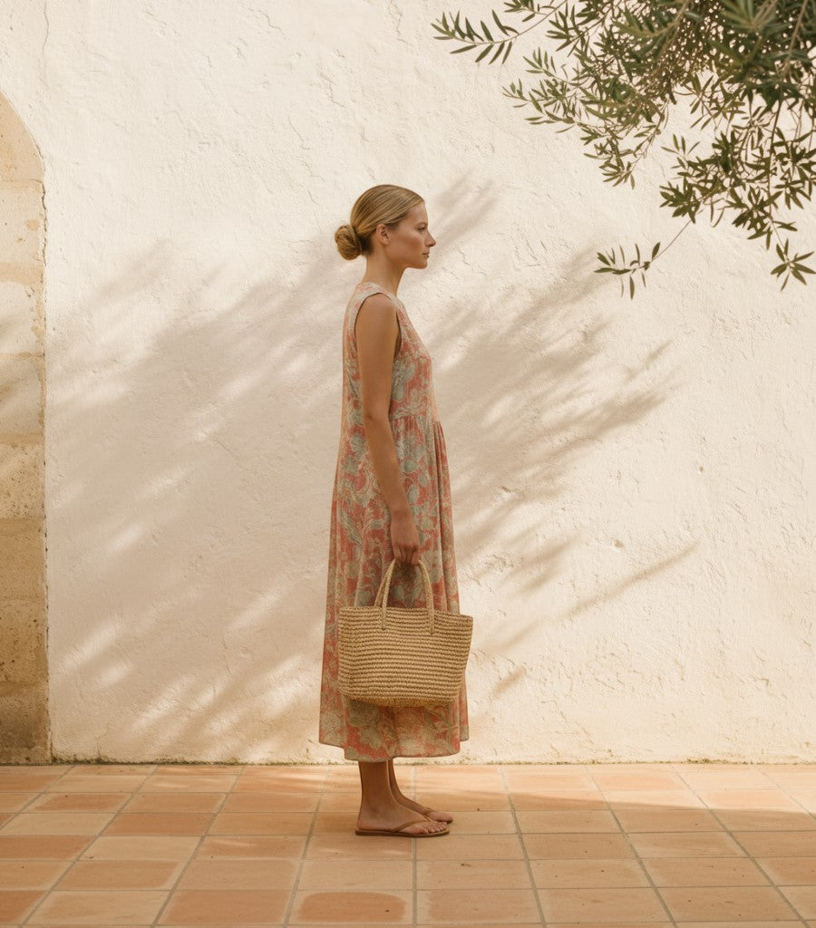 Modelo de perfil con vestido midi Clarvyna estampado en tonos suaves, tejido de algodón y viscosa, con bolso de rafia.